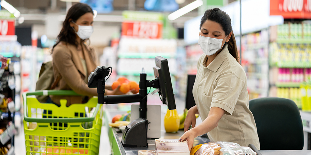 A cashier in a mask scans a woman's groceries 