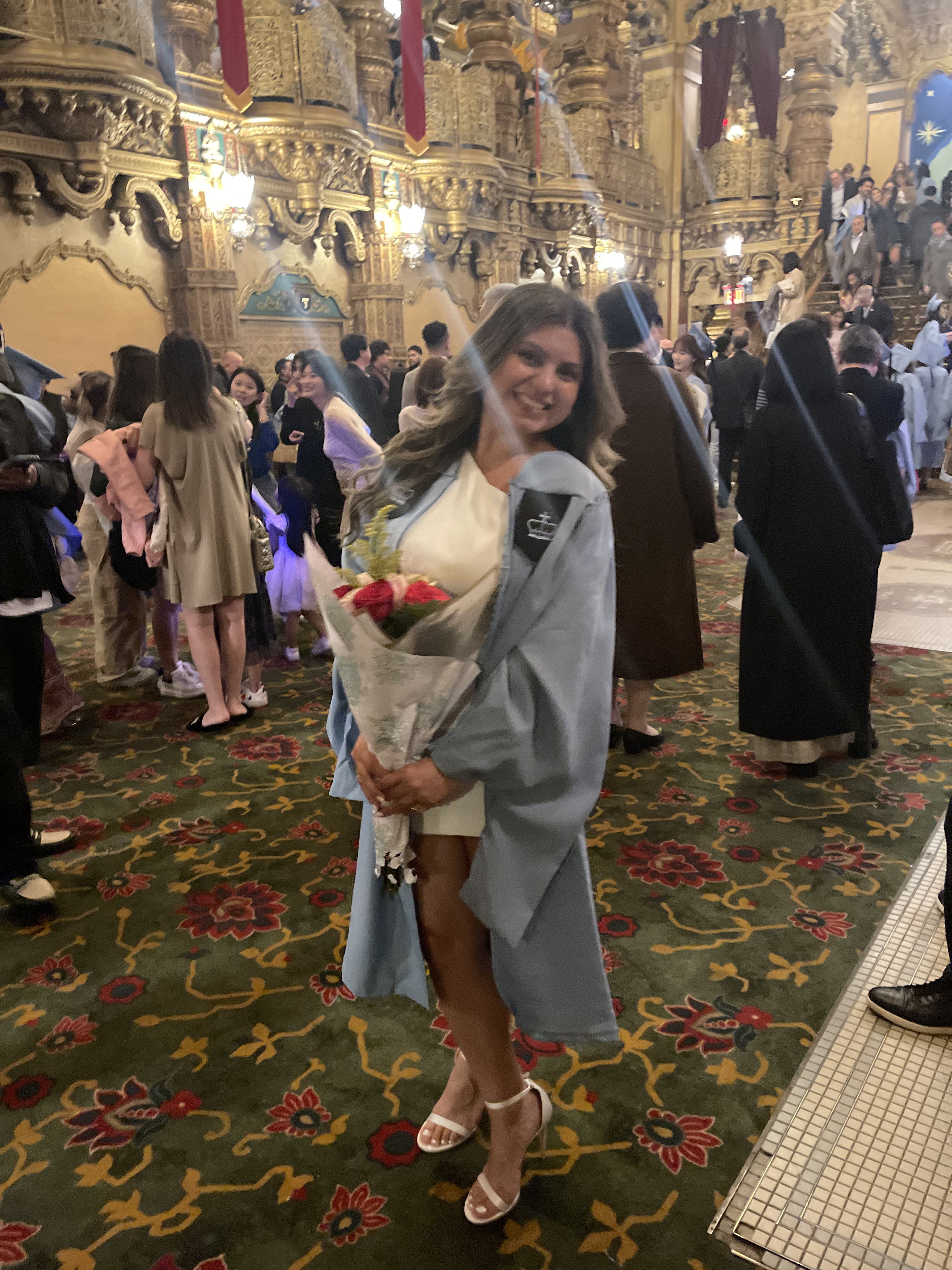 Image of Jenivee Gastelum in graduation robes holding flowers