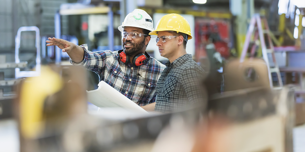 Two men in hardhats talk in a factory