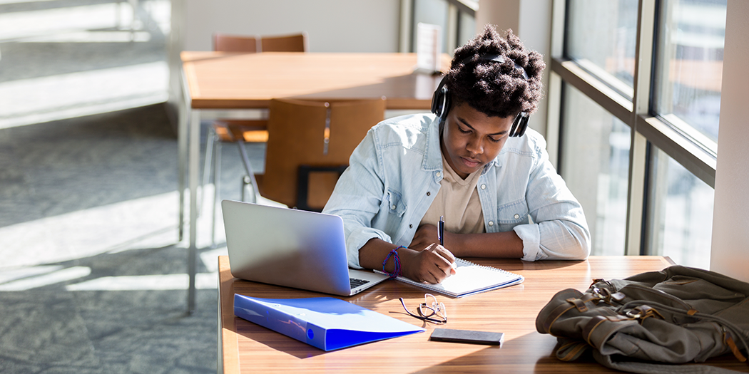 A student studies on his laptop with headphones on