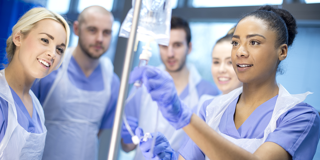 A group of nursing students gathers around an IV bag